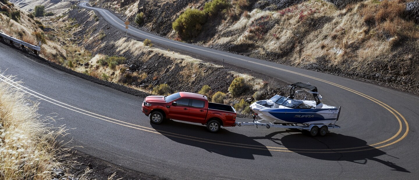 2021 Ford Ranger in Rapid Red Metallic Tinted Clearcoat on a curved road towing a boat