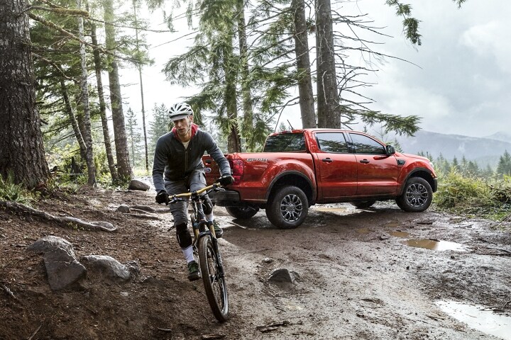 2023 Ford Ranger® in Hot Pepper Metallic parked in woods with cyclist pedalling away