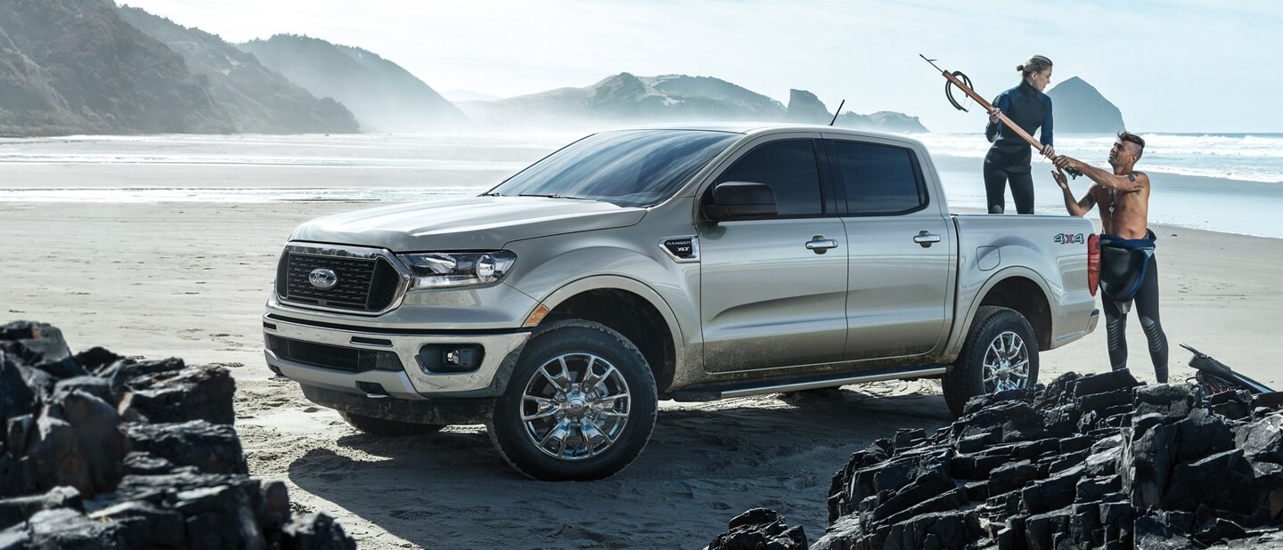 2023 Ford Ranger® parked on a rocky beach with surfers loading gear into the box