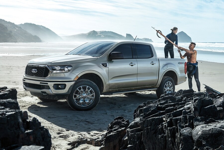 2023 Ford Ranger® parked on a rocky beach with surfers loading gear into the box