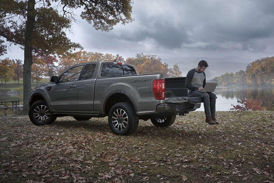 A man sitting on the tailgate of the 2023 Ford Ranger® in Carbonized Grey parked by a lake