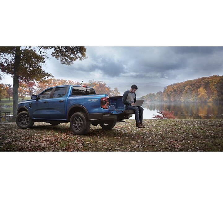 A person with a laptop in the bed of a 2024 Ford Ranger® in a scenic location