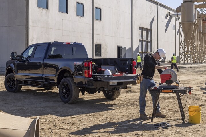 Man using a miter saw at a worksite with a 2023 Ford Super Duty® parked nearby with tailgate down