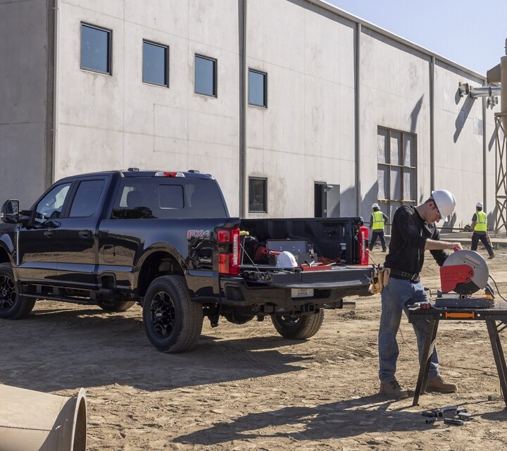 Man using a miter saw at a work site with a 2023 Ford Super Duty® truck parked nearby with tailgate down