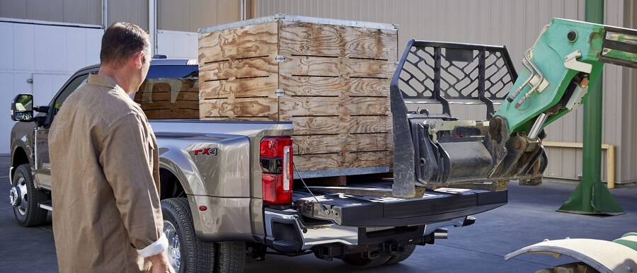 A forklift loading a pallet into the bed of a 2023 Ford Super Duty® F-350 Lariat with a man standing next to it