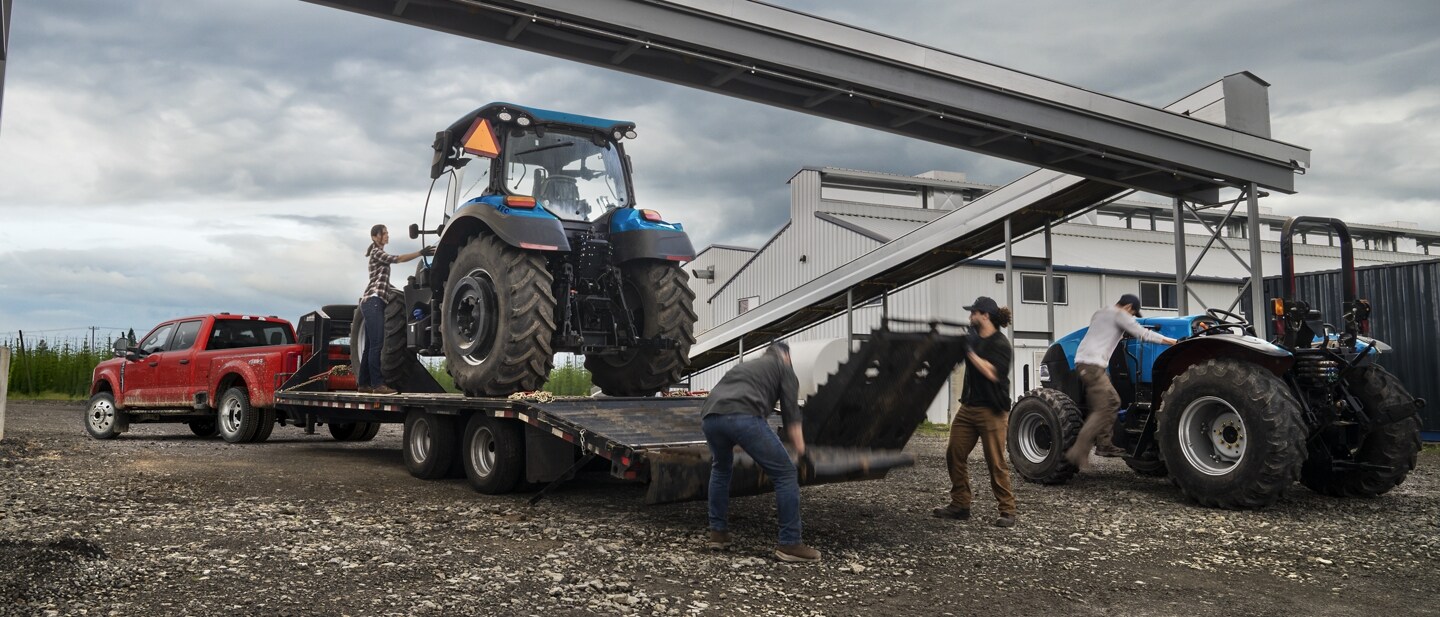 Men loading a tractor onto a trailer hitched to a 2023 Ford Super Duty® F-450® XL SuperCrew® Cab near a grain factory