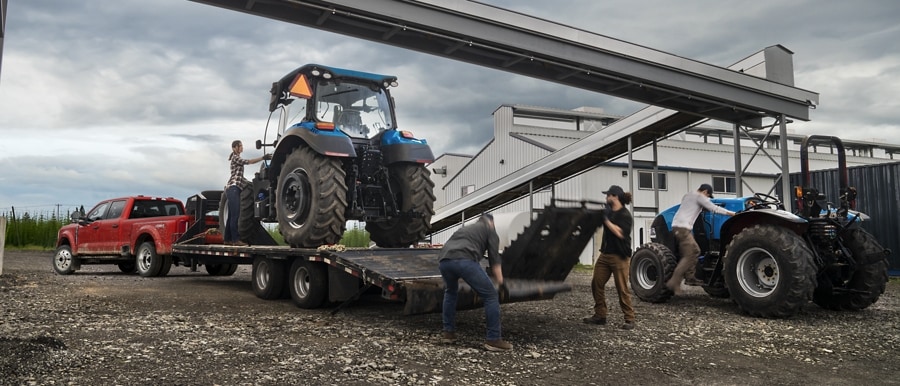 A tractor being loaded onto a trailer hitched to a 2023 Ford Super Duty® F-450 XL Super Crew Cab near a grain factory