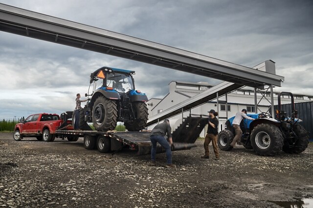 Men loading a tractor onto a trailer hitched to a 2023 Ford Super Duty® F-450® XL SuperCrew® Cab near a grain factory