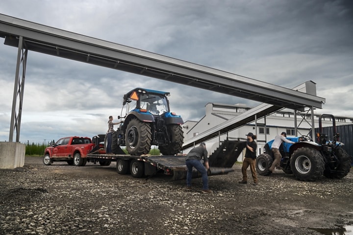 A tractor being loaded onto a trailer hitched to a 2023 Ford Super Duty® F-450 XL Super Crew Cab near a grain factory