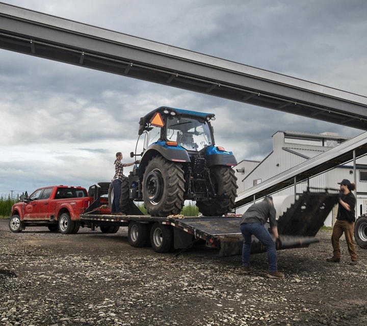 Men loading a tractor onto a trailer hitched to a 2023 Ford Super Duty® F-450 XL SuperCrew® Cab near a grain factory
