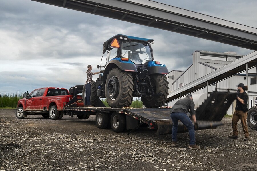 A tractor being loaded onto a trailer hitched to a 2023 Ford Super Duty® F-450 XL Super Crew Cab near a grain factory