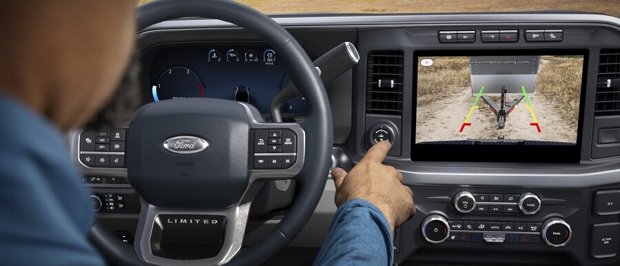 A person pushing the pro trailer backup assist knob with camera image and guidelines displayed on screen