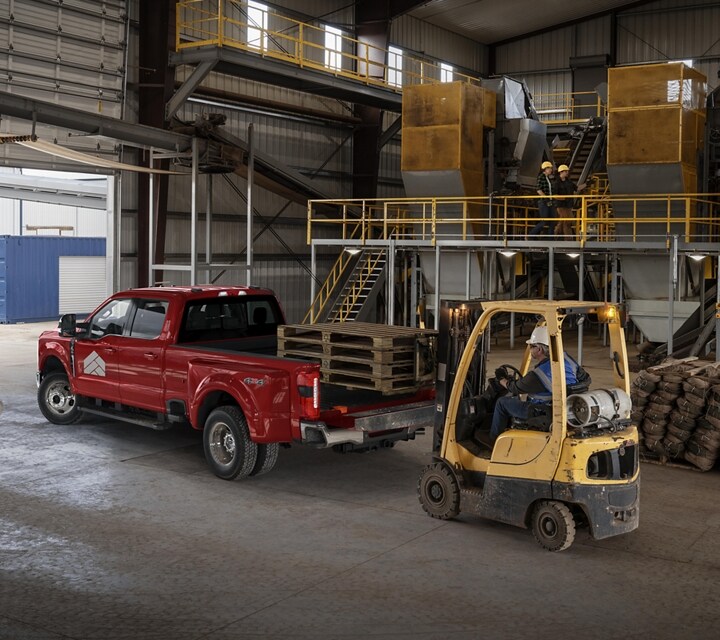 Man watching a forklift loading pales of hay into the bed of a 2025 Ford Super Duty® LARIAT® pickup