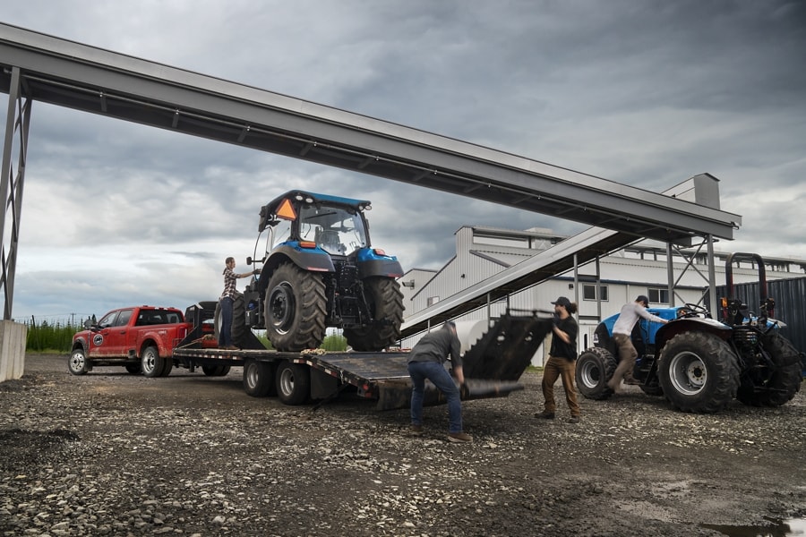 People loading a large tractor onto a trailer hitched to a 2025 Ford Super Duty® F-450® XL DRW truck in Rapid Red