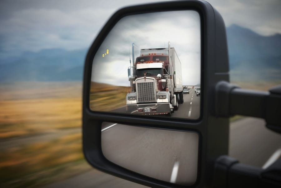 Close-up of the side view mirror showing a semi-truck in the reflection and the BLIS® alert icon