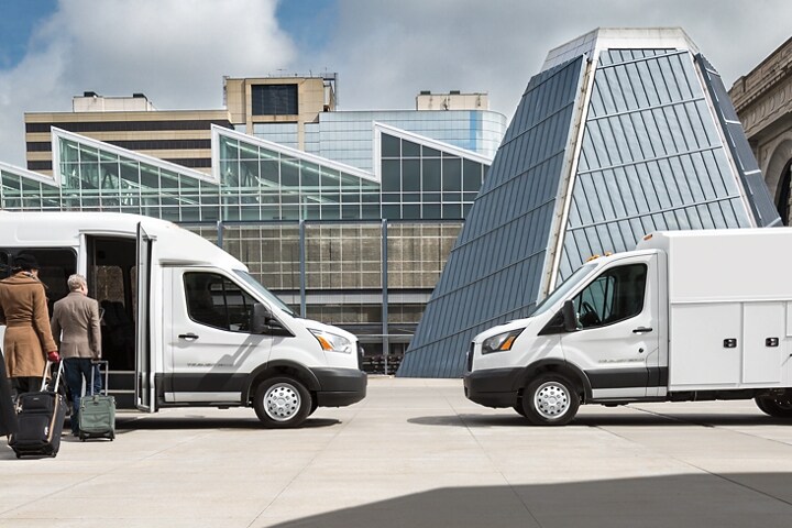 People with luggage entering a 2024 Ford Transit® model with Shuttle Bus upfit parked facing another Transit® model