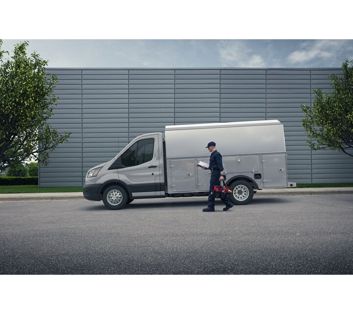 Person carrying tools walking near a 2024 Ford Transit® Chassis Cab model with mechanic's truck upfit