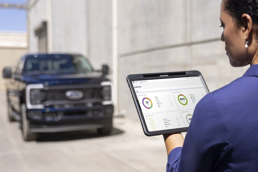 An individual looking over metrics on a tablet with a 2025 Ford Super Duty parked in the background