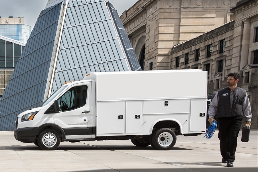 A person walking near a 2025 Ford Transit® model parked in a city carrying work supplies