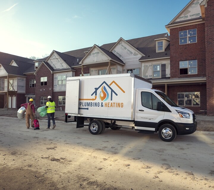 Two workers standing near a 2025 Ford Transit® model with box truck upfit parked at a construction site