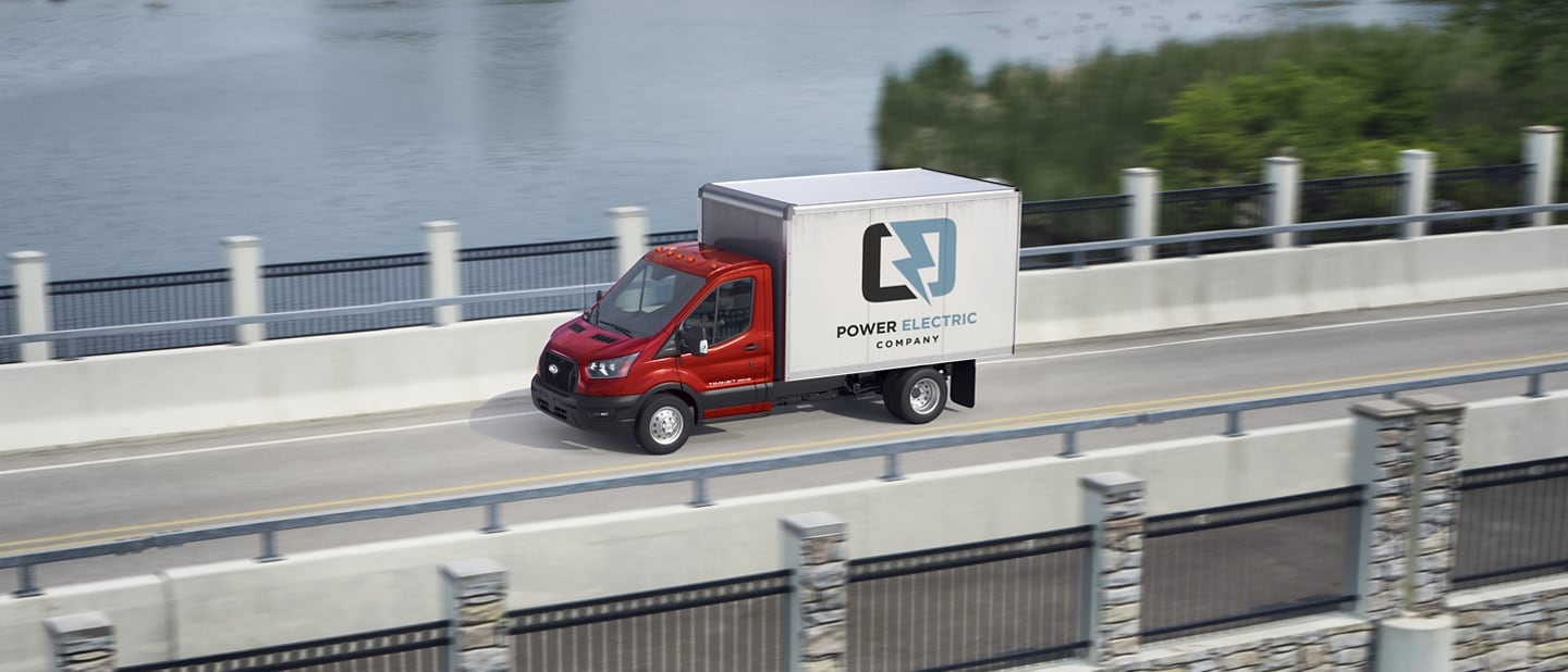 2025 Ford Transit® Chassis Cab model with box truck upfit being driven over a bridge with a lake in the background