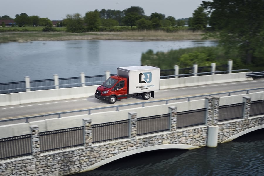2025 Ford Transit® Chassis Cab model with box truck upfit being driven over a bridge with a lake in the background