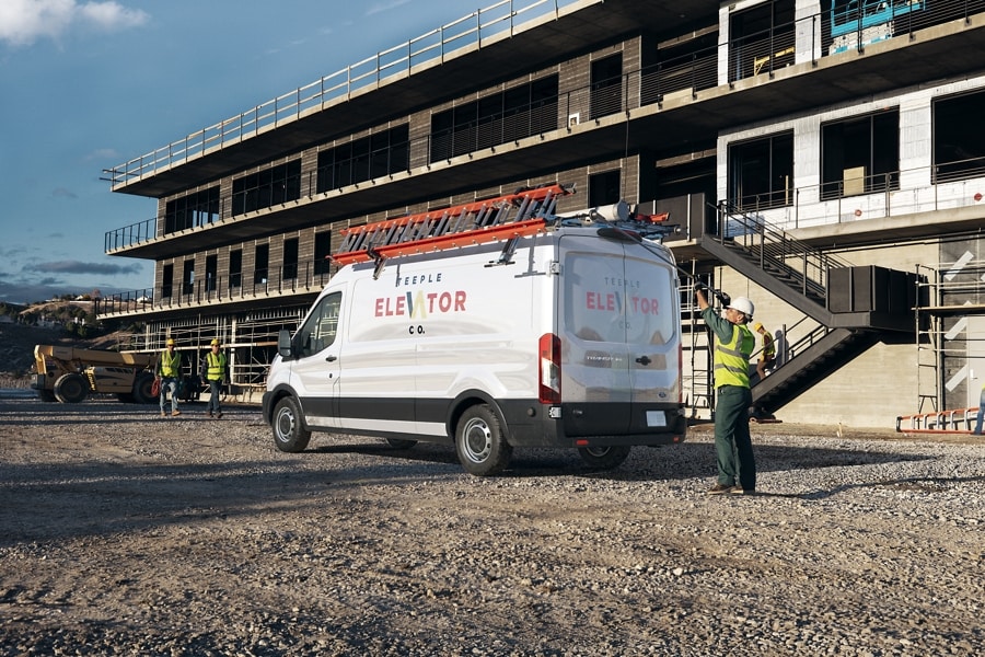 A man unloading equipment from the top of a Ford Transit® Van at a construction site