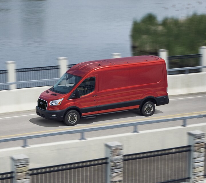 A 2023 Ford Transit® Van in Race Red being driven across a bridge