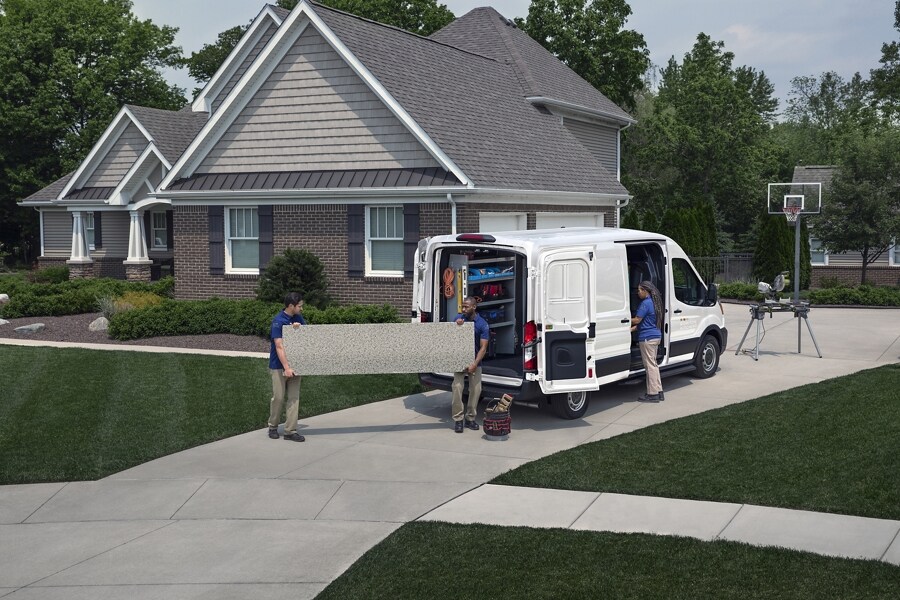 A 2023 Ford Transit® Van parked at a home with 2 men outside and a woman standing at an open side door