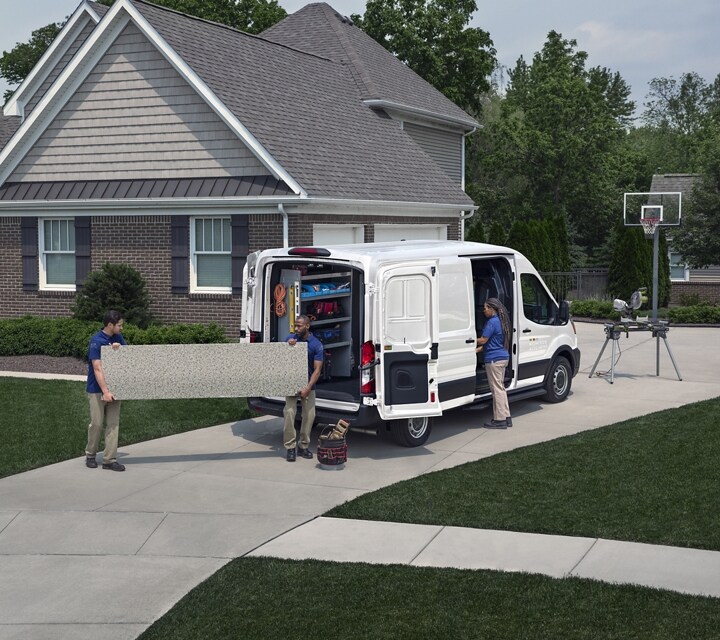 Rear view of a 2023 Transit® Cargo Van parked in a driveway with the side and rear cargo doors open