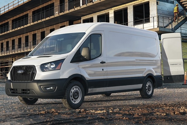 Two men at a construction site talking in the foreground while someone unloads items from a 2023 Ford Transit® Van