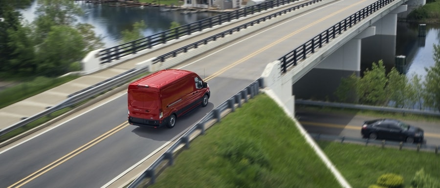 A 2024 Ford Transit® van in Race Red being driven across a bridge