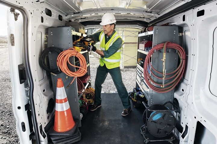 A worker stands in the back of a 2024 Ford Transit® van surrounded by electric cords, tools, shelves and more
