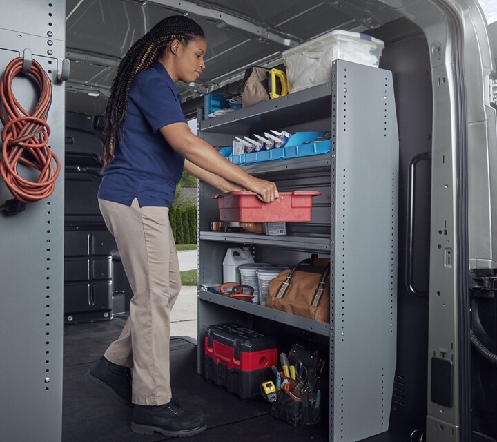A person in the cargo area of a 2024 Ford Transit® van outfitted with bins and racks