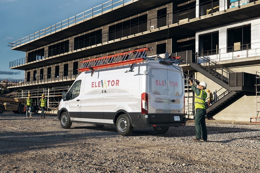 A 2024 Ford Transit® van parked at a construction site with a worker standing at the rear doors
