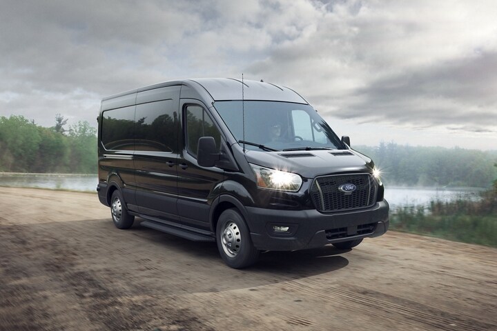 A 2024 Ford Transit® van in Agate Black with Intelligent All-Wheel Drive travels down a dirt road