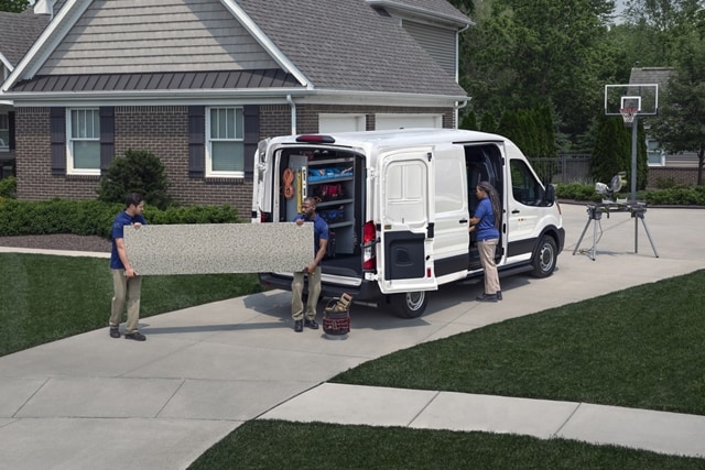 Two workers unloading a length of big, heavy granite from a 2025 Ford Transit® van