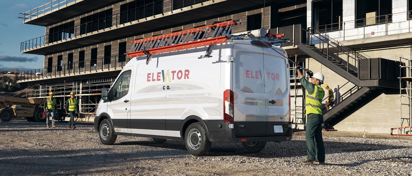 A 2025 Ford Transit® van parked at a construction site with a worker standing at the rear doors