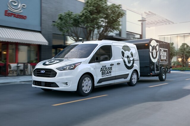 2023 Ford Transit Connect Cargo Van in Frozen White towing a trailer through the city