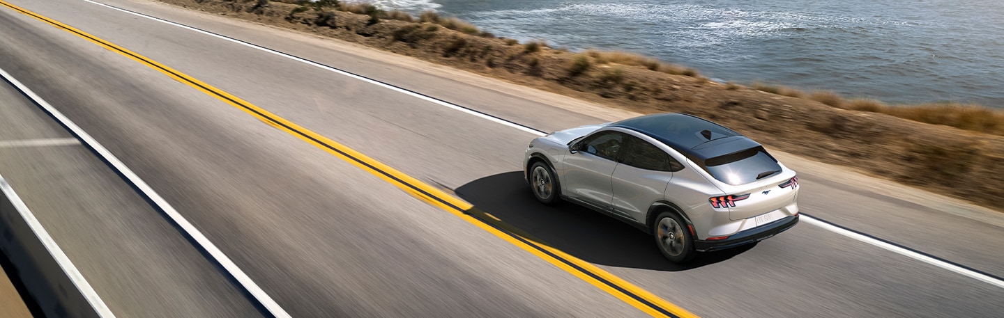 Overhead view of a 2021 Ford Mustang Mach E Premium being driven along a coastal mountain road