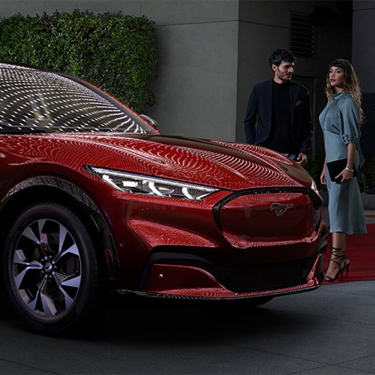 A couple standing near a 2022 Ford Mustang Mach-E on a red carpet